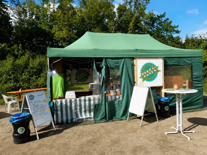 Der grüne Pavillon des PSV-Pizza-Teams mit Angebotstafel und Stehtisch auf dem Festplatz